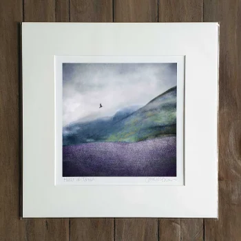a Hills of Tweed mounted print propped up against a dark grey wall. The print is an abstract picture of a Scottish hillside with a bird flying above in the distance. There is a tweed texture in the foreground.