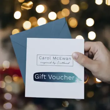 a hand holding a card which says Carol McEwan inspired by Scotland gift voucher. There are twinkly lights int he background