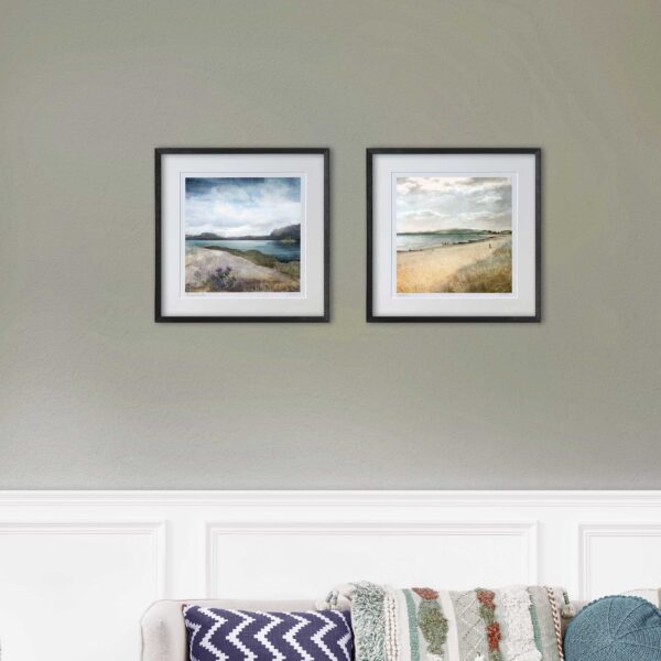 A green wall with 2 prints hanging in black frames. One print is Plockton Thistles and the other print is Broughty Ferry Beach. In the foreground there's white panelling on the wall and a sofa with jazzy cushions on it.