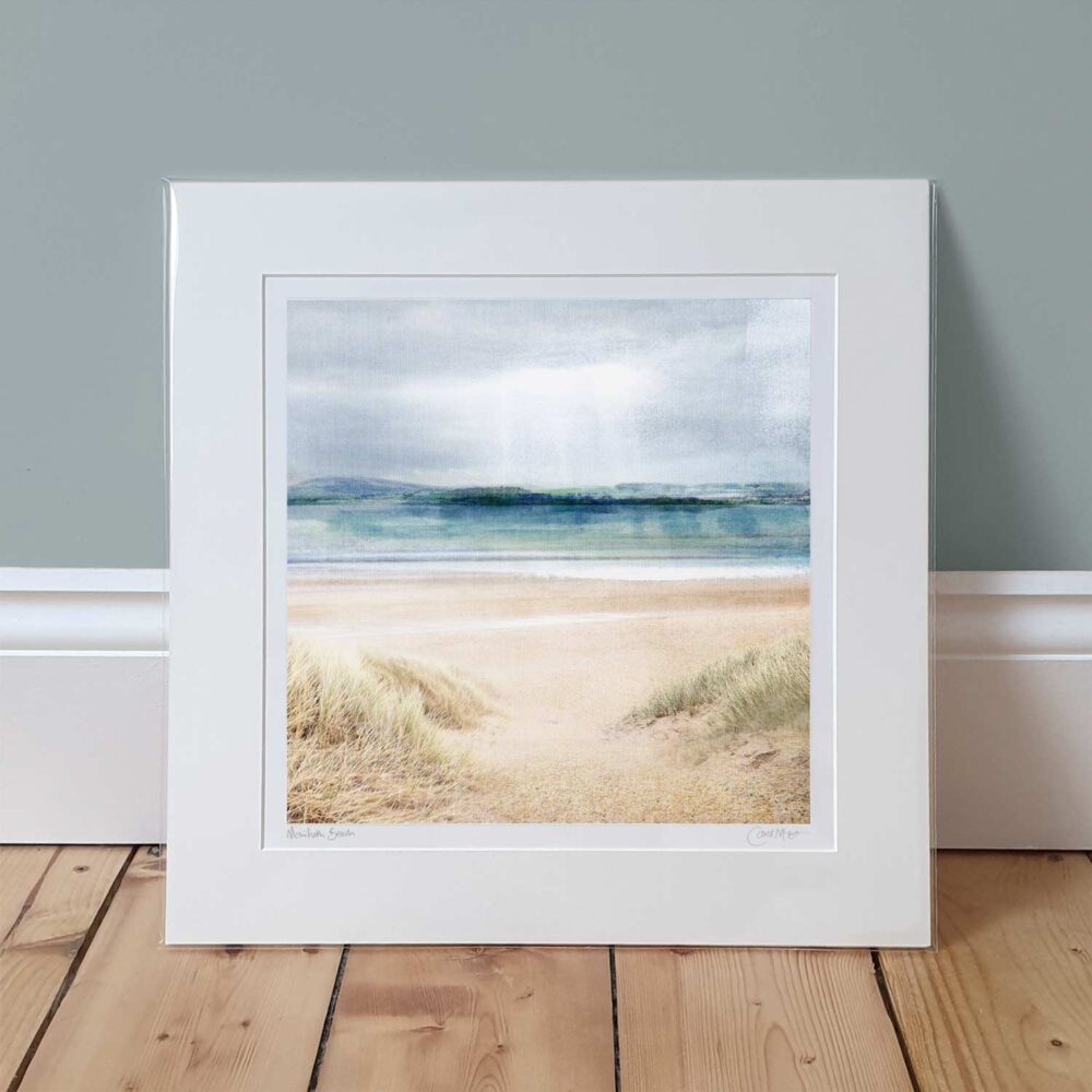 A mounted print of Monifieth Beach leaning against a pale green wall. The colours in the print are light and pale colours of a beach in summer, with a pale, cloudy sky.