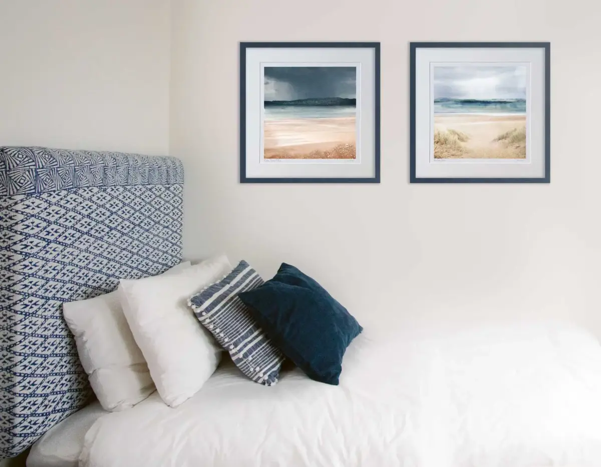 A bedroom with a bed and on the wall behind is 2 Carol McEwan art prints. The beach prints are in navy blue frames to match the pillows and headboard