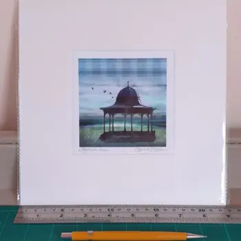 a 9 inch square print of Magalden Green with tartan pattern in the print and floral pattern on the grass. The print is propped against a wall with a ruler and pencil in front of it.