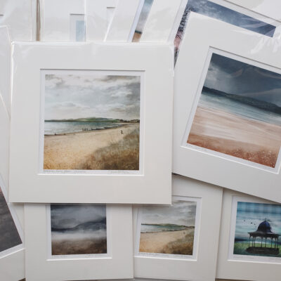 lots of mounted art prints randomly scattered about. They are square shaped in 2 different sizes. The ones on top are beach prints which have blues and greens in the colours as well as the colour of sandy beaches.