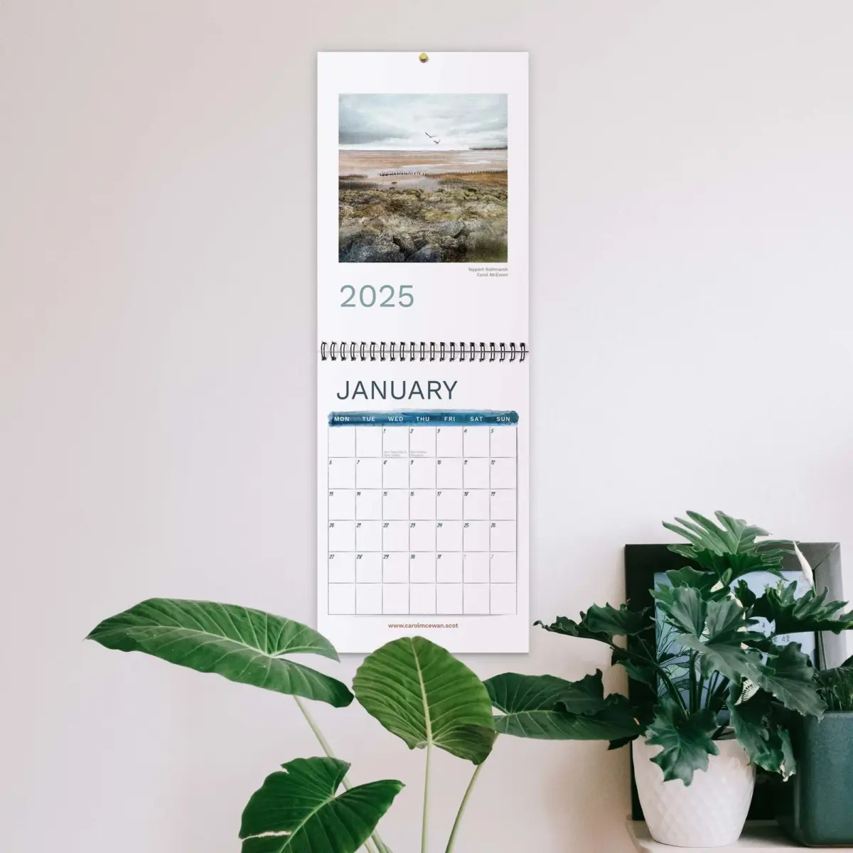 a calendar on a beige wall with houseplants in the foreground