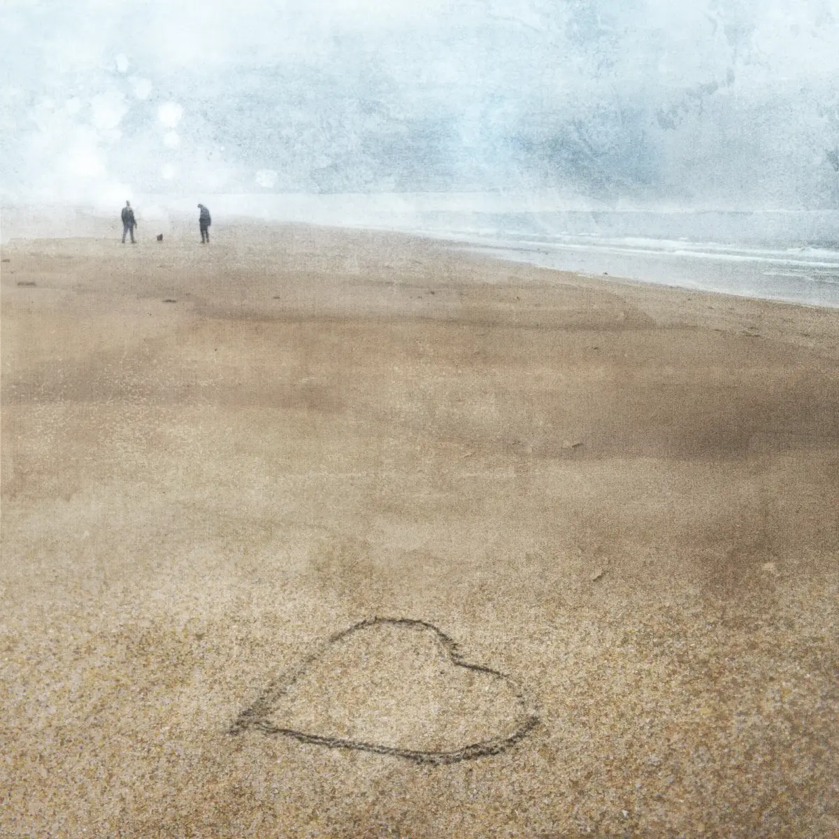 Beach Walk - 2 people in the distance walking their dog no a beach in the rain with a loveheart drawn in the sand